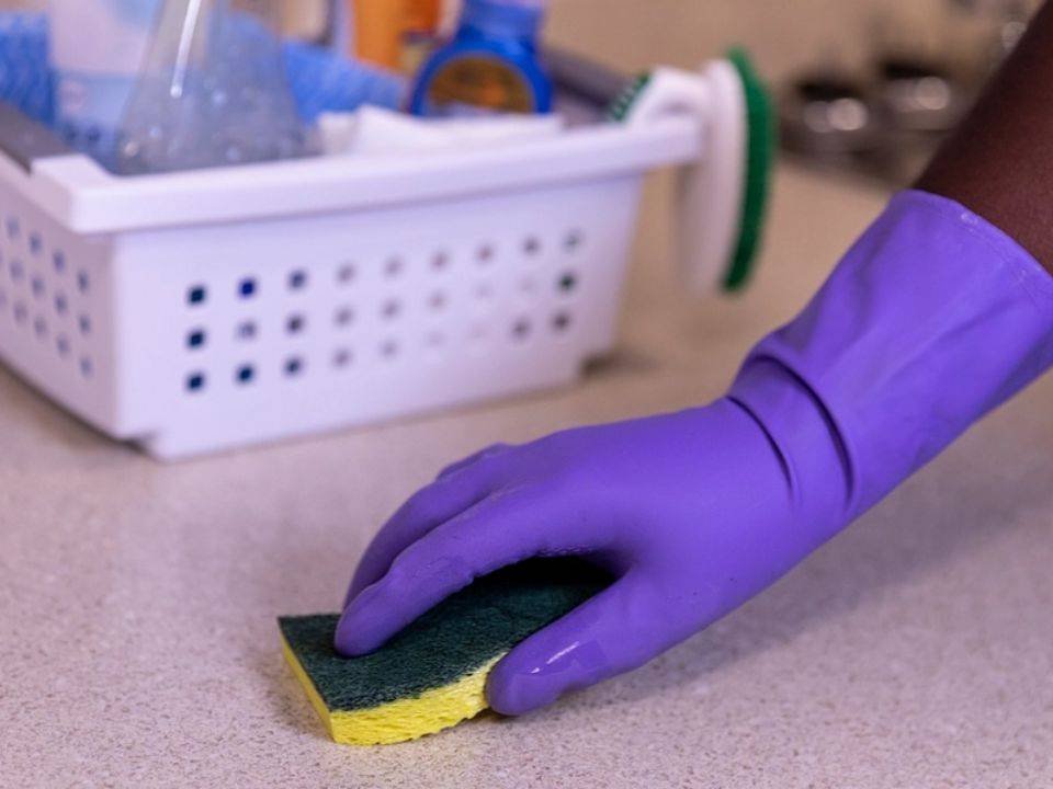 Cleaner wiping a surface with gloves and a sponge